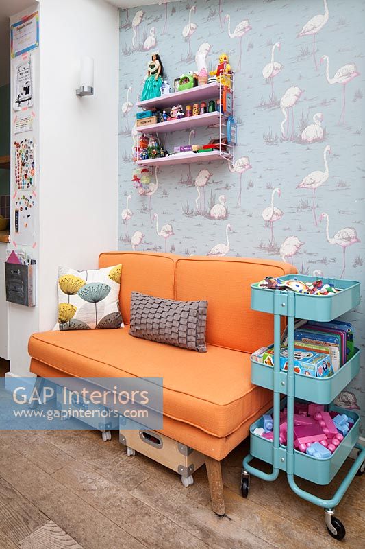 Flamingotapete und orange Sofa im bunten Kinderzimmer