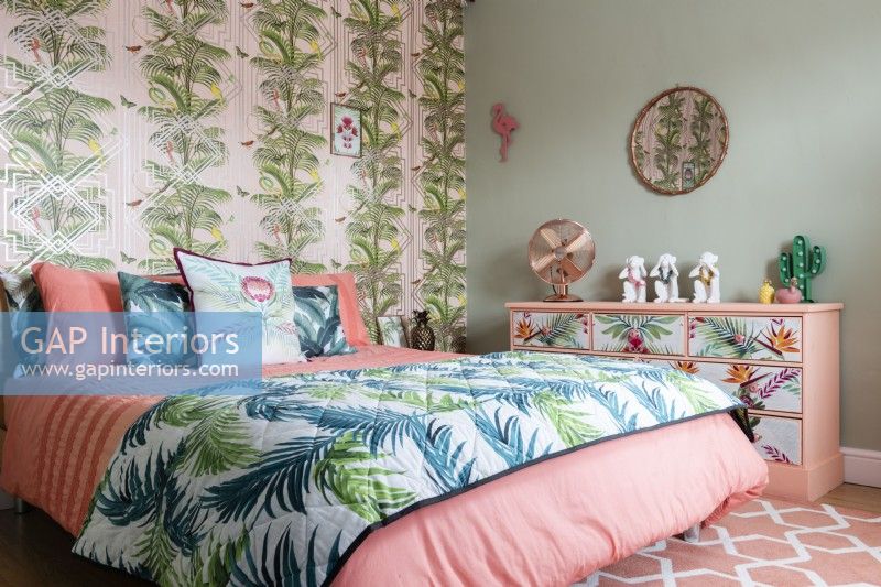 Modernes Schlafzimmer mit palmengemusterter Tapete und Tagesdecke und floral bemalter Kommode