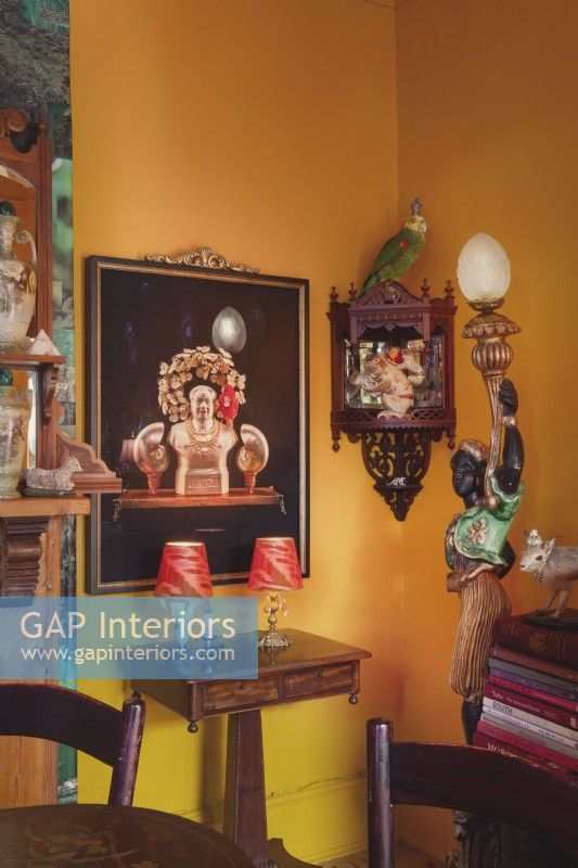 Corner of dining room with yellow wall, eclectic ornaments and art