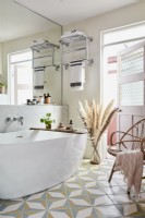 Badezimmer mit ovaler Badewanne und Fliesenboden, rosa Spiegelwandtür, Korbsessel