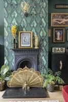 Schwarzer viktorianischer Kamin mit grün gemusterter Art-Déco-Tapete und dekorativem Feuerschutz mit goldenem Pfauenfächer