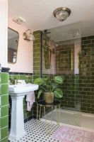Weißes Waschbecken und Duschkabine in einem grün gefliesten und blassrosa Badezimmer