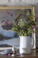 Vase mit Wildblumen auf einer Kommode, dahinter alte maritime Malerei und weiß getünchte Wände